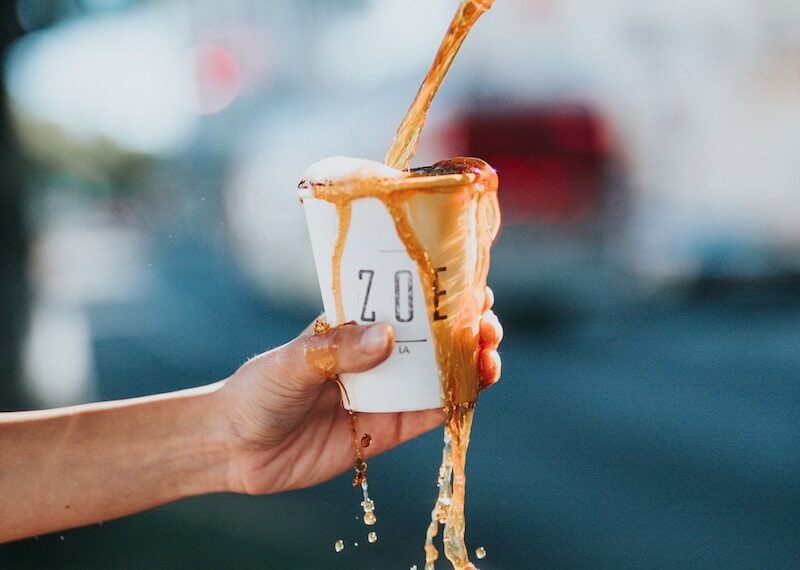 person holding white ZOE brand paper cup