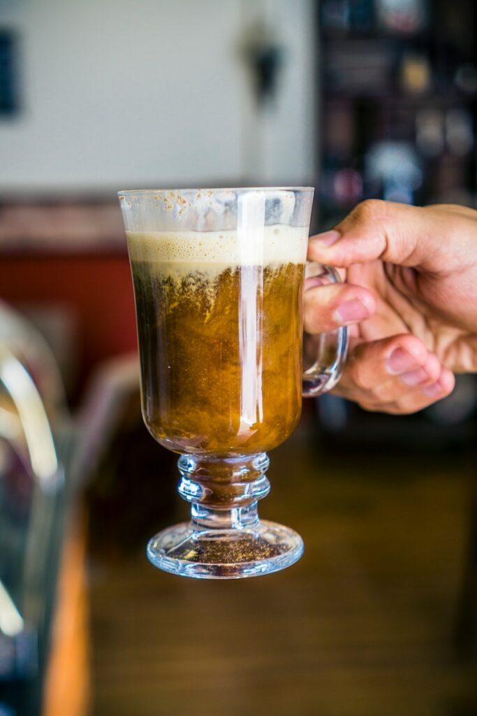 person holding glass mug with brown liquid