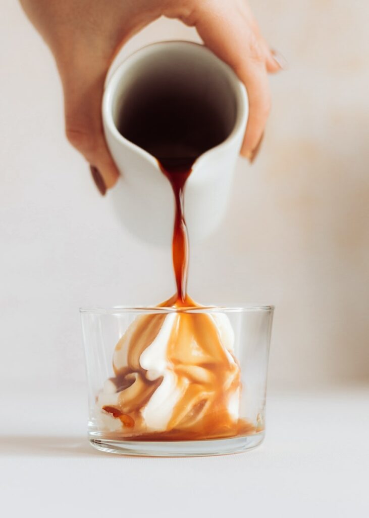 a person pouring caramel sauce into a glass