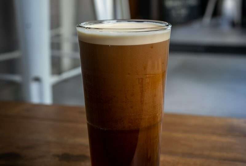a glass filled with nitro coffee sitting on top of a wooden table